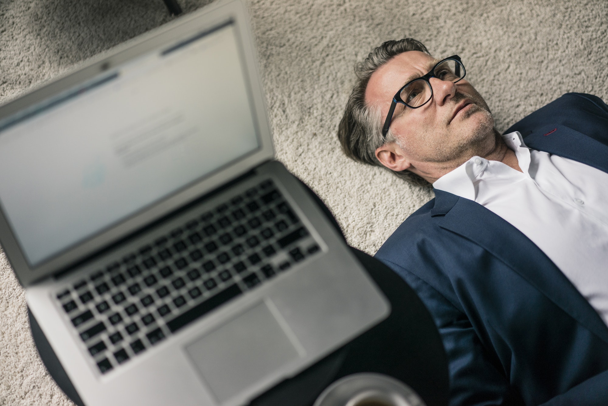 Mature businessman lying on carpet next to laptop Mature businessman lying on carpet next to laptop
